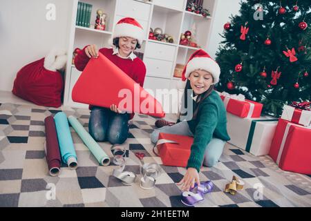 Photo de beau rêve enfants emballage papier paquet santa atelier concept porter x-mas chapeau pull dans la maison décorée à l'intérieur Banque D'Images