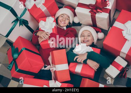 Photo de très adorables petits enfants couché plancher embrasser présent boîte porter x-mas chapeau pull dans la maison décorée à l'intérieur Banque D'Images