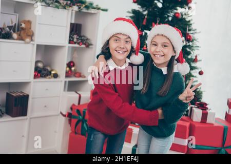 Photo de paisible et sincère enfants embrasser profiter de l'atmosphère de la veille porter x-mas chapeau pull dans la maison décorée à l'intérieur Banque D'Images