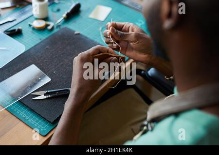 Gros plan sur un homme afro-américain méconnu qui crée un sac en cuir fait main tout en travaillant dans un atelier de maroquinerie, espace de travail Banque D'Images