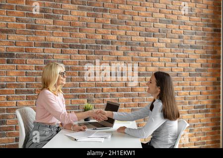 Des femmes qui se secouent la main au bureau.Travail d'équipe, partenariats et concept d'embauche.Une agente de recrutement d'âge moyen interroge une jeune femme au bureau, chercheuse d'emploi Banque D'Images