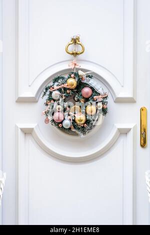 Vue avant d'une couronne de Noël en branches de sapin en plastique avec boules et rubans, accrochée sur une porte avant blanche avec moulures. Banque D'Images