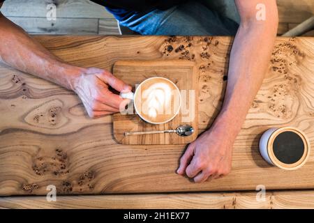 Les mains du Mans tiennent une tasse de cappuccino sur une table en bois dans le café.Au-dessus, vue de dessus, plan d'affichage, espace de copie Banque D'Images