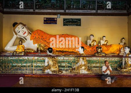 YANGON, MYANMAR - 3 JANVIER 2014: Homme méditant près de la statue du Bouddha couché dans la pagode Shwedagon Paya Banque D'Images