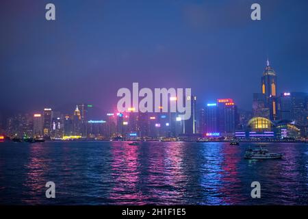 HONG KONG, CHINE - 28 AVRIL 2018 : le paysage urbain de Hong Kong s'étend sur le port de Victoria le soir, illuminé par un bateau touristique Banque D'Images