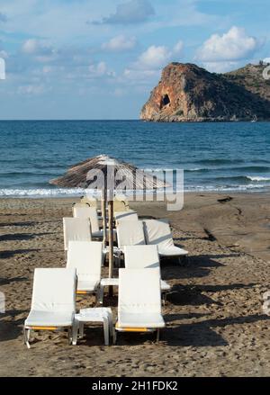 Agia Marina, Chania Crete magnifique scène grecque plage chaises longues sur le sable vue verticale avec vue îlot rocheux Banque D'Images