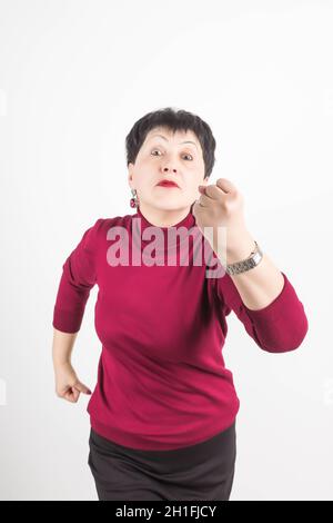Photo de la femme en colère frobas visage, montre poing, a insatisfait expression du visage, porte des vêtements rouges décontractés, menaces sur quelque chose, isolé sur whi Banque D'Images