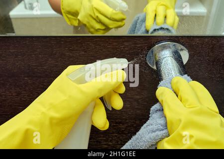 L'homme nettoie la salle de bains en essuyant le robinet du lavabo avec un chiffon.Désinfection avec des gants en caoutchouc jaune dans les toilettes Banque D'Images