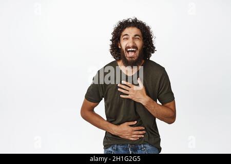 Portrait d'un homme du Moyen-Orient heureux riant, souriant et riant de quelque chose de drôle, debout dans un t-shirt sur fond blanc Banque D'Images