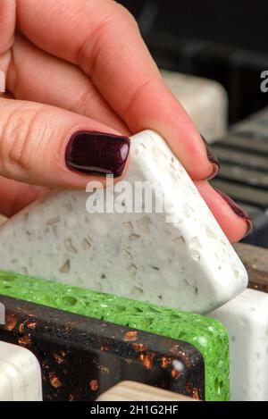 Une femme choisit des échantillons de pierre pour un comptoir de cuisine.Un ensemble d'échantillons multicolores de pierre artificielle acrylique. Banque D'Images