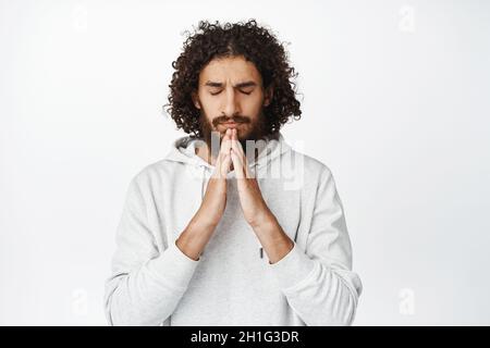 Un homme hispanique inquiet plein d'espoir qui priait, pleurant dieu, espérant le sourire, se tenant sur fond blanc Banque D'Images