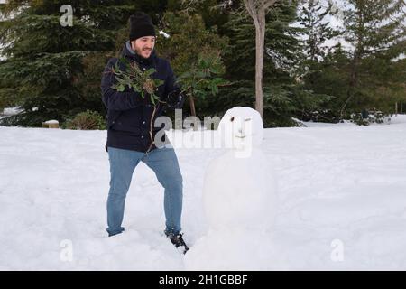 Un jeune homme caucasien faisant un smiley bonhomme de neige nuit avec des branches Banque D'Images