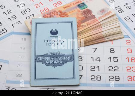 Anapa, Russie - 29.06.2020: Sur un paquet de cinq millièmes billets russes se trouve un livre d'épargne, un fond de feuilles de calendrier Banque D'Images