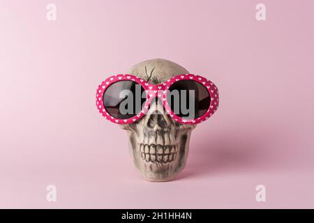 Tête de crâne d'Halloween avec lunettes de soleil sur fond rose.Concept de vacances minimal. Banque D'Images