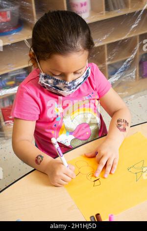 Éducation préscolaire 3-4 ans art activité fille dessin bonhomme de neige figure avec marqueur, la tenant avec poignée trépied, portant masque facial Banque D'Images