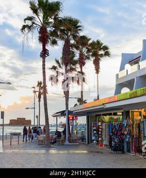 PAPHOS, CHYPRE - 15 FÉVRIER 2019: Centre-ville touristique avec boutiques de souvenirs et cafés, voiture, palmiers et coucher de soleil sur la mer Banque D'Images