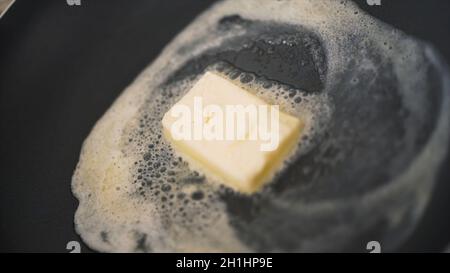 Gros plan d'un morceau de beurre fondu dans une poêle à frire.Action.Faire cuire dans une poêle avec un morceau de beurre fondu.Le beurre gras fond dans une casserole chaude. Banque D'Images