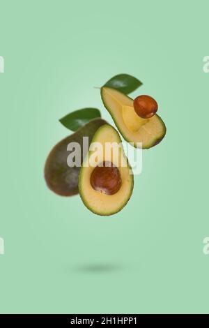 Scène créative avec avocat entier mûr frais et tranché volant dans l'air isolé sur fond vert clair.Alimentation saine, alimentation, fruits exotiques tropicaux, Banque D'Images