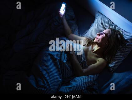 Jolie femme d'âge moyen, en utilisant son téléphone portable au lit à la maison avant de dormir Banque D'Images