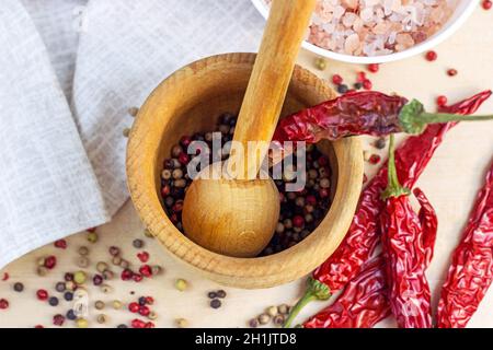 Vue de dessus des grains de poivre séchés mélangés dans le mortier avec pilon, poivre sec au piment et sel pour cuisiner sur fond de planche à découper en bois clair dans le k Banque D'Images