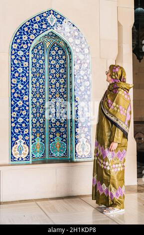 Une femme habillée dans une abaya omanaise traditionnelle qui regarde une alcôve ornée à la grande mosquée du Sultan Qaboos à Muscat, Oman Banque D'Images