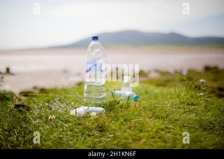 Photo d'un couple de bouteilles en plastique lité abandonnées sur l'herbe avec une terre ouverte floue et une montagne en arrière-plan Banque D'Images