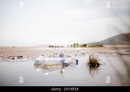 Vue panoramique de quelques bouteilles en plastique vides sur une flaque dans le sable avec le ciel bleu clair comme arrière-plan Banque D'Images