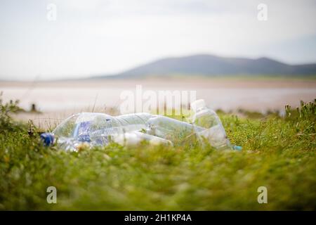 Photo d'un couple de bouteilles en plastique vides abandonnées sur l'herbe avec un terrain ouvert flou et une montagne en arrière-plan Banque D'Images