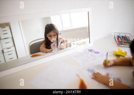 Paysage image d'un miroir sur une table blanche reflétant une petite fille dans une robe rose colorant différents types de feuilles sur une feuille de papier, avec Banque D'Images