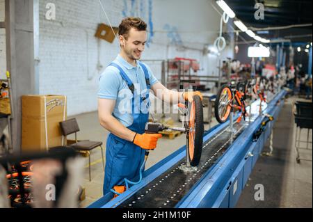 Usine de bicyclettes, travailleur à la chaîne de montage, installation de la chaîne.Un mécanicien d'uniforme de sexe masculin installe des pièces de cycle dans l'atelier, la fabrication industrielle Banque D'Images