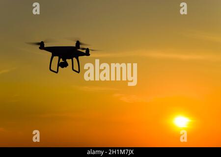 Silhouette Quadrocopters contre l'arrière-plan de la coucher du soleil. Drones volant dans le ciel du soir. Banque D'Images