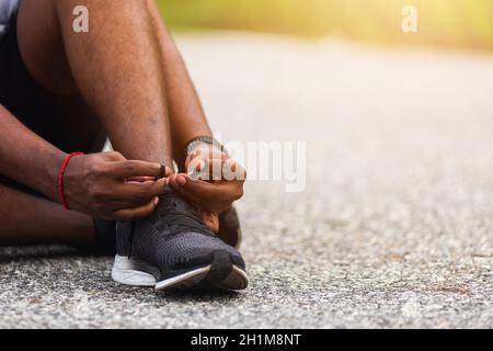 Gros plan asiatique coureur sportif noir homme assis chaussures de course à pied essayer des chaussures de course à pied se préparer pour le jogging et courir dans la rue extérieure, exercice de santé W Banque D'Images