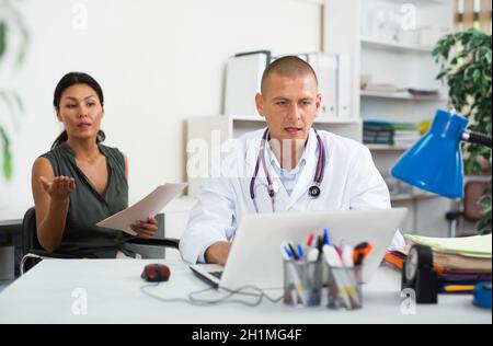 Médecin écrivant la prescription à la patiente sur ordinateur portable à la clinique Banque D'Images