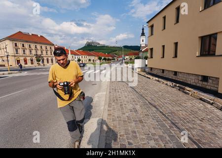 Jeune touriste avec caméra sur la route à proximité de maisons colorées et sur fond du château de Spas en Slovaquie. Banque D'Images