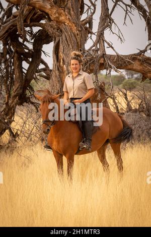 Blonde à cheval par arbre mort torsadé Banque D'Images