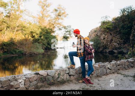 Un homme chauve avec une barbe et une fille blonde dedans des chapeaux brillants sur le fond de la rivière sont pris photos avec un ancien appareil photo Banque D'Images