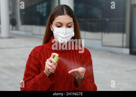 Portrait d'une jeune femme portant un masque médical de protection pulvérisant de l'alcool assainisseur sur ses mains dans la rue moderne de la ville Banque D'Images