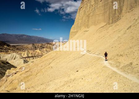 Femme marche le long de Thin Trail en traversant les pentes des Badlands de la Vallée de la mort sur le sentier du canyon doré Banque D'Images