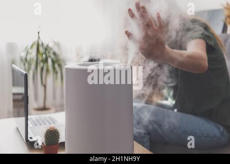 Femme freelance utilise un humidificateur domestique sur le lieu de travail pour maintenir l'humidité relative et le microclimat sur le lieu de travail du bureau à domicile avec Banque D'Images