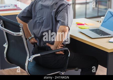Un homme d'affaires asiatique expérimenté travaillant avec un ordinateur portable a un problème avec les maux de dos. Le vieil homme ressent de la douleur après s'être assis longtemps à son bureau, Healthc Banque D'Images