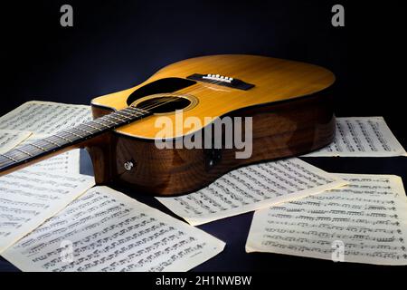 feuilles avec partitions musicales et guitare acoustique classique jaune à six cordes avec un pickguard noir sur un arrière-plan noir isolé Banque D'Images
