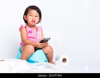 Asiatique petite mignonne bébé fille éducation entraînement à s'asseoir sur pot bleu de chambre ou pot et jouer smartphone mobile avec des rouleaux de papier de toilette, goujon Banque D'Images