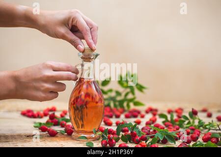 Deux ballons de verre de fermeture des mains de femme contenant de l'huile essentielle de rosehip avec bouchon de liège.Concept de médecine alternative à base de plantes.Baies rouges coulées o Banque D'Images