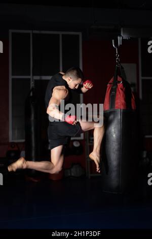 Un chasseur de kickboxing qui exécute des coups de poing avec un sac de punch Knee on.Homme caucasien pratiquant la formation d'arts martiaux à Urban Gym.Phot de haute qualité Banque D'Images