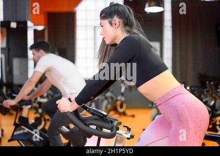 Belle femme à vélo sur un vélo de fitness moderne pendant un cours de patinage de groupe à la salle de gym. Photo de haute qualité Banque D'Images