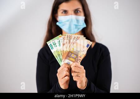 Femme heureuse tenant plusieurs billets de banque et portant un masque facial en studio.Portrait d'une femme adulte gaie avec de longs cheveux bruns et de l'argent entre ses mains Banque D'Images