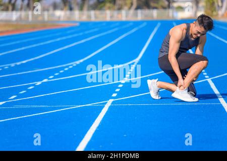 jeune homme souffrant de douleurs soudaines aux chevilles et aux jambes pendant l'entraînement au stade Banque D'Images