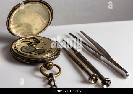 Antiquités, montre de poche suisse vintage, deux tournevis et une pince à épiler se trouvent sur une table en plastique blanc Banque D'Images