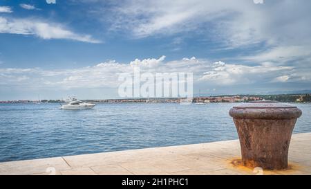 Bateau à moteur naviguant dans la baie de Zadar et simple, vieux et rouillé bollard de mouillage sur la jetée. Mer Adriatique et côte de la ville de Zadar, Croatie Banque D'Images