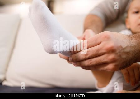 Le jeune père met des chaussettes sur son fils, assis sur un canapé. Banque D'Images